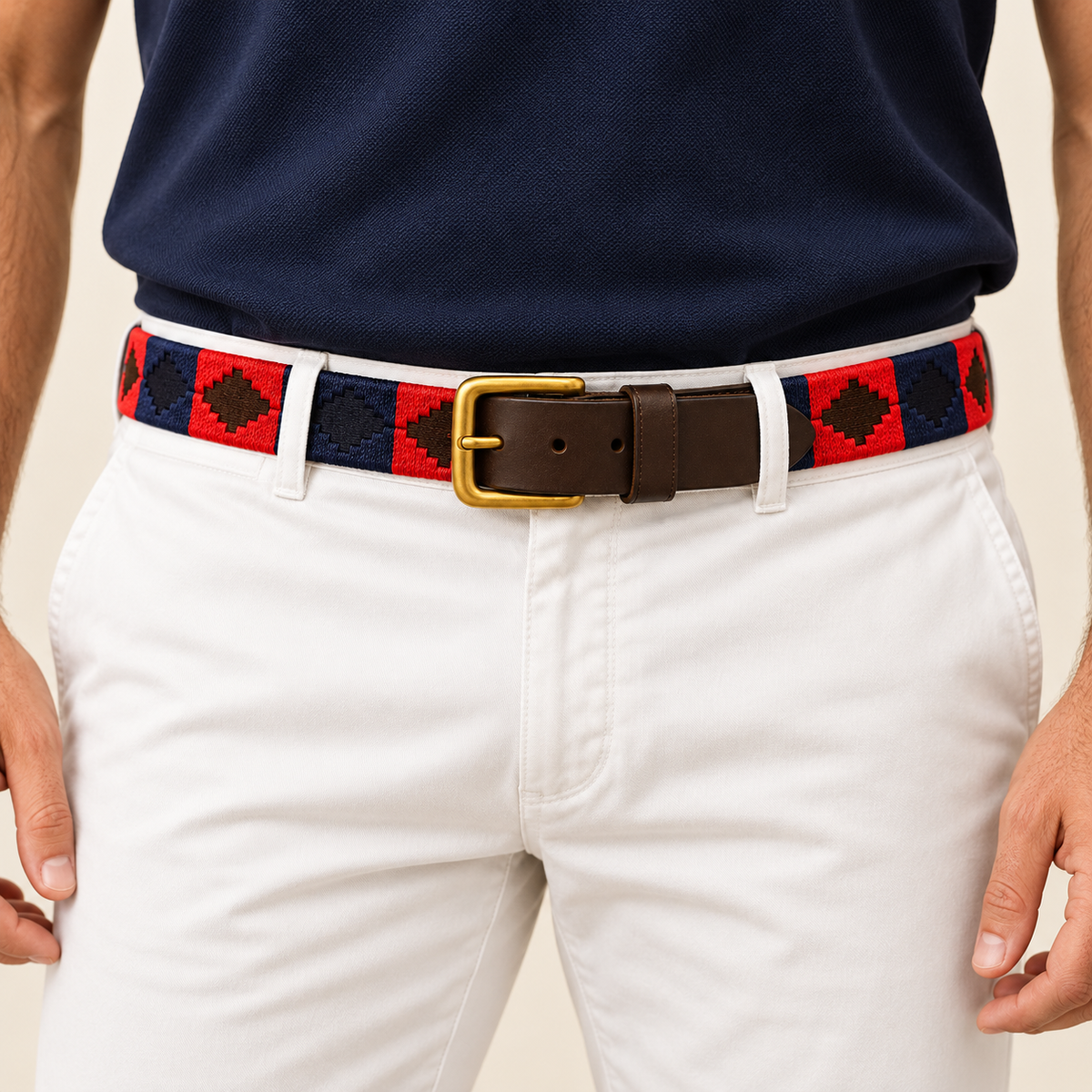 Red and navy handmade handwoven gaucho polo belt with brown leather and brass buckle worn with white trousers and a navy polo shirt.